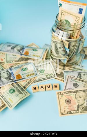 Geld in internationaler Währung, einschließlich des Euro, liegt der Dollar auf blauem Hintergrund neben einem Glas mit Banknoten und der Inschrift außer. Stockfoto