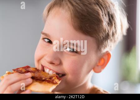 Happy teen boy genießen köstliche Pizza zu Hause essen. Porträt eines niedlichen Teenagers Stockfoto