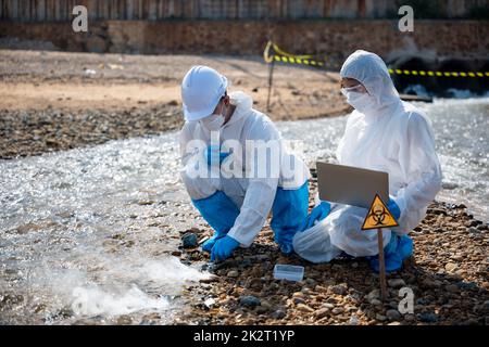 Biologe tragen Schutzanzug und Maske sammelt Abwasserproben aus der Industrie Stockfoto