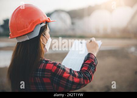 Glückliche asiatische Arbeiterin in der Ölchemie Arbeiterin, die eine visuelle Inspektionsliste auf dem Klemmbrett in der Fabrik arbeitet Stockfoto
