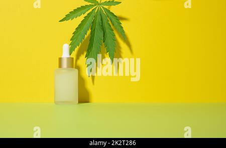 Weiße Glasflasche mit Pipette und grünem Cannabisblatt auf gelbem Hintergrund Stockfoto