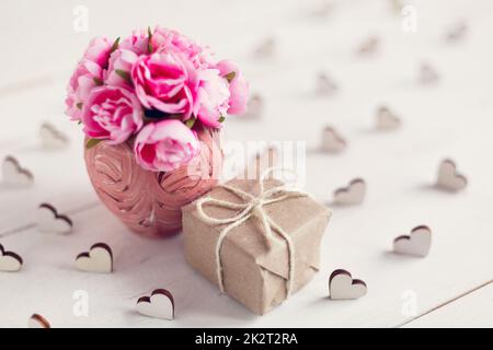 Kleine rosa Rosen in einer schönen Vase und ein kleines Geschenk in Kraftpapier verpackt. Stockfoto