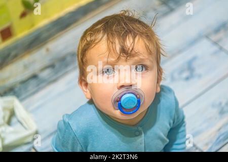 Weißer Junge mit blauen Augen mit einem Schnuller im Mund schaut nach oben Stockfoto