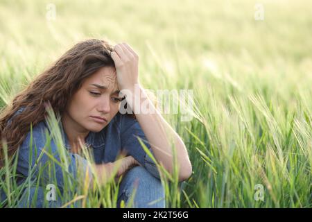 Traurige Frau, die sich auf einem Feld beschwert Stockfoto