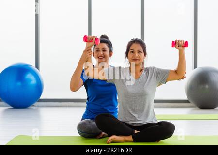 Eine Lehrerin unterrichtet eine Erwachsene Schülerin, die Yoga-Hände mit Kurzhanteln macht Stockfoto