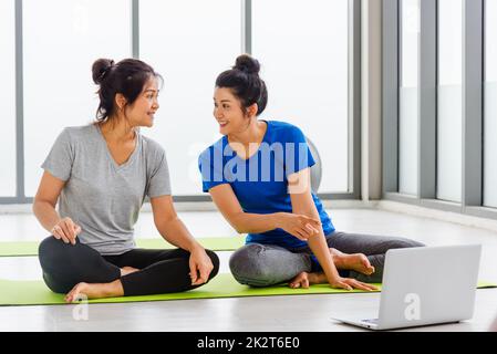 Erwachsene und junge Frauen in Sportbekleidung, die auf dem Fußboden sitzen und ein Notebook für das Training suchen Stockfoto