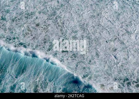 Ein wunderschöner Blick auf eine blaue Meereslandschaft mit Surfern, die bei Tageslicht Wellen fangen Stockfoto