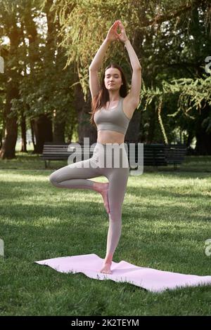 Eine junge positive Frau im Turnanzug praktiziert Yoga und meditiert, während sie auf einer Matte sitzt. Stockfoto