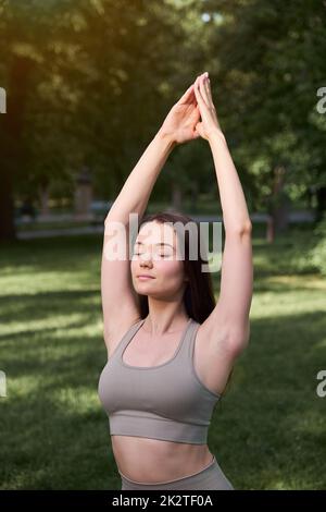 Porträt einer glücklichen jungen Frau, die an einem Sommertag im Park Yoga praktiziert. Stockfoto