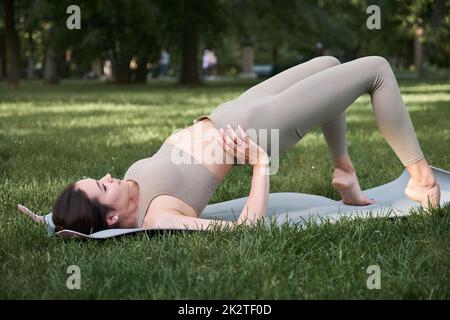 Eine junge positive Frau im Turnanzug praktiziert Yoga und meditiert, während sie auf einer Matte sitzt. Stockfoto