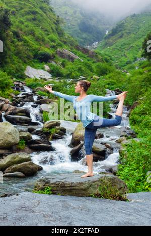 Frau tut Yoga Asana Natarajasana im Freien am Wasserfall Stockfoto