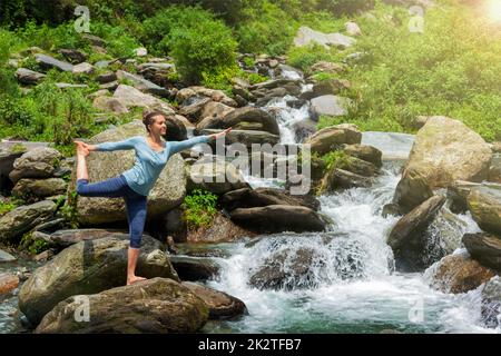 Frau tut Yoga Asana Natarajasana im Freien am Wasserfall Stockfoto