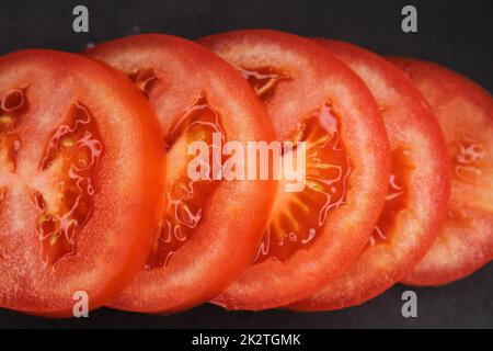 Nahaufnahme von Tomatenscheiben auf schwarzem Hintergrund. Blick von oben. Stockfoto