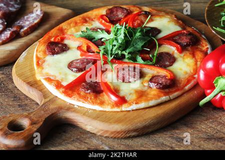 Hot hausgemachte Pizza mit Salami, paprica, Rucola auf hölzernen Tisch Stockfoto