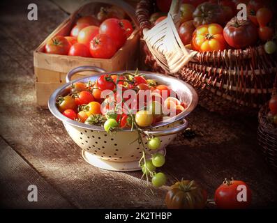 Verschiedene Heirloom Tomaten in Körben auf rustikalen Tisch. Bunte Tomaten - rot, gelb, orange. Ernte Gemüse kochen Konzeption Stockfoto