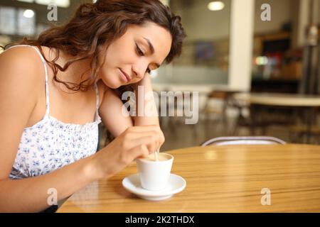 Nachdenkliche Frau, die Kaffee rührt, sitzt in einem Restaurant Stockfoto