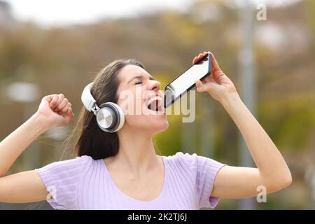 Fröhliche Teenager, die auf der Straße singen und das Telefon als Mikrofon benutzen Stockfoto