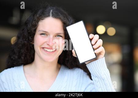 Glückliche Frau, die vor der Kamera einen leeren Handybildschirm zeigt Stockfoto