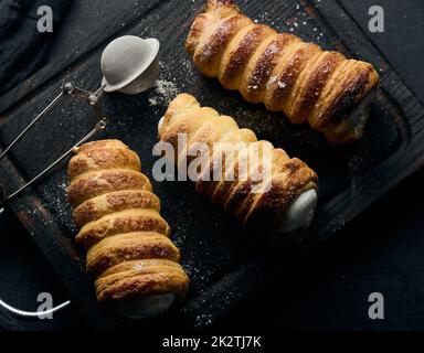 Gebackene Tubuli gefüllt mit geschlagener Eiweiß-Creme auf einem schwarzen Küchenbrett aus Holz Stockfoto