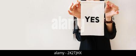 Junge Geschäftsfrau in einem schwarzen Anzug zeigt eine weiße Plakatwand auf einem weißen, isolierten Hintergrund. Auf dem Poster steht ja. Konzept für Unternehmen und Werbung. Banner. Stockfoto