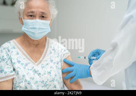 Ältere asiatische ältere Frau, die Gesichtsmaske trägt, erhält von einem Arzt eine Covid-19- oder Coronavirus-Impfung. Stockfoto