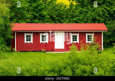 Rotes Holzhaus in einer Natur mit vielen grünen Bäumen und Rasen Stockfoto