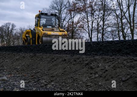 Nahaufnahme einer Straßenwalze, die auf einer neuen Straßenbaustelle arbeitet. Stockfoto