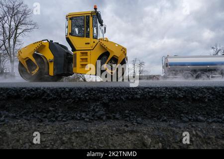 Nahaufnahme einer Straßenwalze, die auf einer neuen Straßenbaustelle arbeitet. Stockfoto