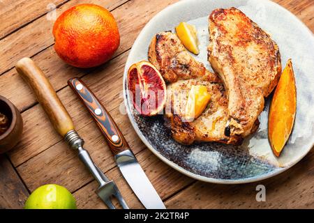 Fleischsteak, appetitliches Schweinekotelett in einer Zitrusmarinade gebraten. Fleisch auf dem Teller auf dem Holztisch Stockfoto