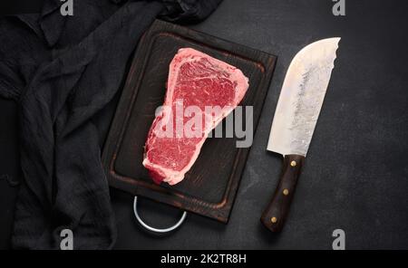 Frisches rohes Stück Rindfleisch, Striploin-Steak auf schwarzem Hintergrund, Draufsicht. Marmoriertes Stück Fleisch Stockfoto