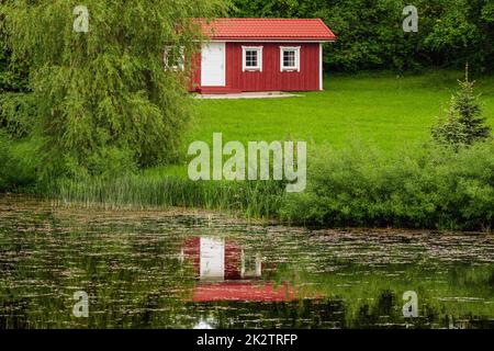 Blick auf rote Ferienhütte mit Reflexion im Teichwasser Stockfoto