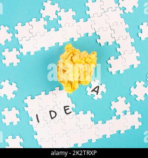 Puzzle auf blauem Hintergrund, gelbes zerbröckeltes Papier, Wortidee steht auf den Puzzleteilen, Brainstomling-Konzept, arbeitet als Team zusammen Stockfoto