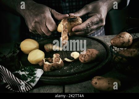 Pflanzen Sie gesichtslose männliche Kartoffeln zum Schälen in der Küche Stockfoto