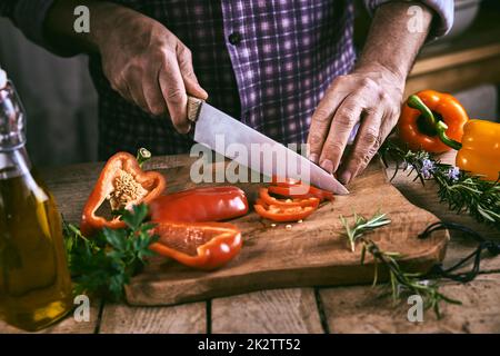 Ein gesichtsloser Mann schneidet Paprika auf dem Schneidebrett in der Küche Stockfoto