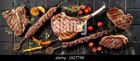 Köstliches gegrilltes Fleisch serviert mit Paprika und Tomaten auf einem schwarzen Tisch Stockfoto