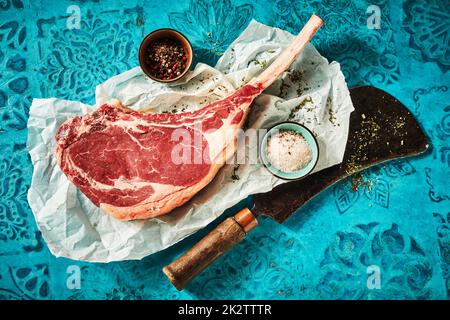 Rohes Tomahawk-Steak mit Gewürzen und Salz auf Papier Stockfoto