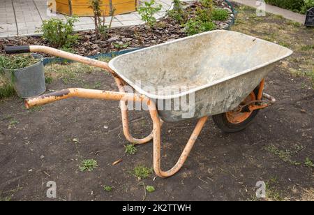 Gartenreinigungsgeräte. Ein leerer Gartenwagen in Nahaufnahme zum Transport von Gülle, Erde und Gras im Garten. Landwirtschaftliche Arbeiten Stockfoto