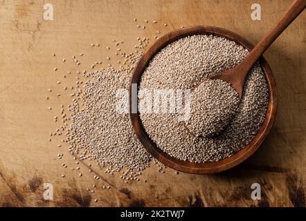 Weiße Chiasamen und Holzlöffel in einer Holzschale auf Holzhintergrund. Stockfoto