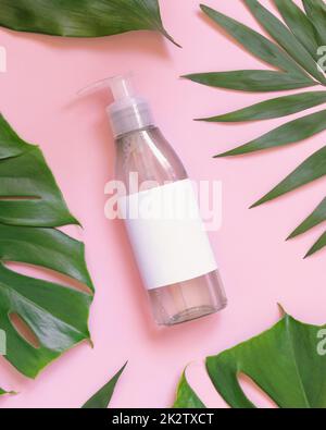 Eine transparente Pumpflasche zwischen tropischen Blättern auf rosafarbener Draufsicht. Verpackungsmodell Stockfoto