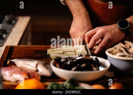 Zerkleinern Sie Sellerie auf Schneidebrett, umgeben von einer Vielzahl von Zutaten. Frische Weichtiere Fischmuschel-Garnelen. Kochen Von Meeresfrüchten. Stockfoto