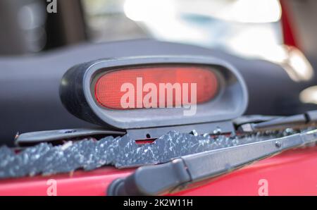 Ein Auto nach einem Unfall mit einer kaputten Heckscheibe. Zerbrochene Scheibe in einem Fahrzeug mit hinterer Bremsleuchte. Wrackteile im Innenraum, detaillierte Nahaufnahme eines beschädigten modernen Autos. Stockfoto