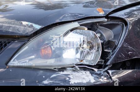 Gebrochene Scheinwerfer infolge einer Kollision. Kaputtes schwarzes Auto nach einem Unfall. Autounfallkonzept. Beschädigter Notscheinwerfer, Motorhaube und Stoßfänger. Schäden an der Karosserie nach dem Unfall. Stockfoto