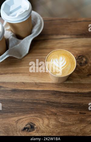 Cappuccino-Kaffee mit wunderschönem Muster auf Schaum in Eco Craft-Glas auf dem Tisch beliebtes Kaffeetassenkonzept. Kaffee zum Mitnehmen. Stockfoto