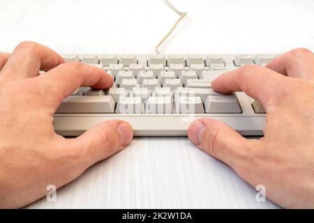 Tippen Sie mit den Händen auf der weißen Tastatur mit Kabel Stockfoto