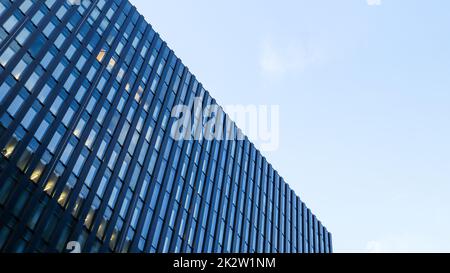 Modernes Hochhaus am blauen Himmel. Blick von unten auf einen Wolkenkratzer im Geschäftsviertel. Blick auf die Glasfassade eines Bürogebäudes aus einem niedrigen Winkel. Stockfoto