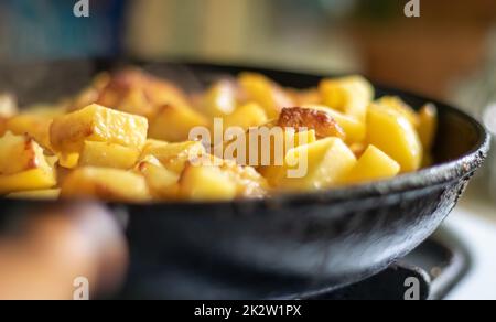 Braten frischer Kartoffeln in einer gusseisernen Pfanne mit Sonnenblumenöl. Blick auf eine Herdplatte mit einer Pfanne gefüllt mit goldenen Bratkartoffeln in einer echten Küche. In einer hausgemachten Bratpfanne gekochtes Essen. Stockfoto