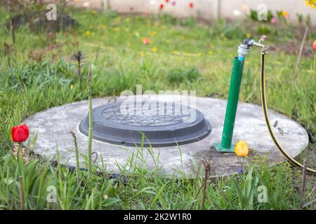 Rohrleitungen, Wasserpumpe aus einem Brunnen. Ein Außenwasserhahn mit einem gelben Gartenschlauch. Bewässerungswasserpumpensystem für die Landwirtschaft. Schlauch im Garten zum Bewässern, sonniger Sommertag. Stockfoto
