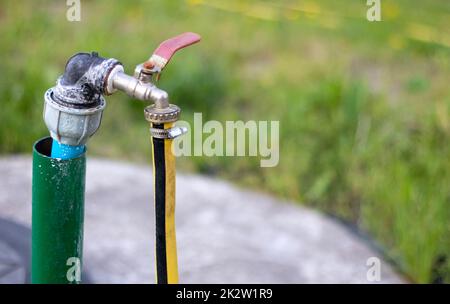 Rohrleitungen, Wasserpumpe aus einem Brunnen. Ein Außenwasserhahn mit einem gelben Gartenschlauch. Bewässerungswasserpumpensystem für die Landwirtschaft. Schlauch im Garten zum Bewässern, sonniger Sommertag. Stockfoto