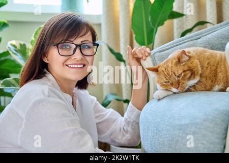 Porträt einer lächelnden Frau mit einer Katze, die auf einem Sessel zu Hause liegt Stockfoto