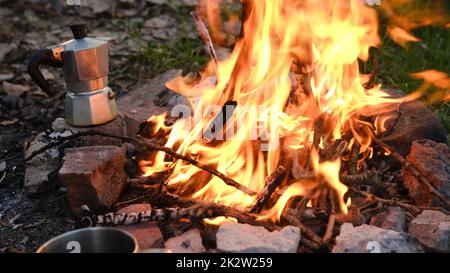 Lagerfeuer im Touristenlager in den Bergen. Wunderschönes Lagerfeuer, brennendes Holz am Sommerabend. Aktives Lifestyle-, Reise-, Wander- und Campingkonzept. Lagerfeuer brennt in Zeitlupe Stockfoto